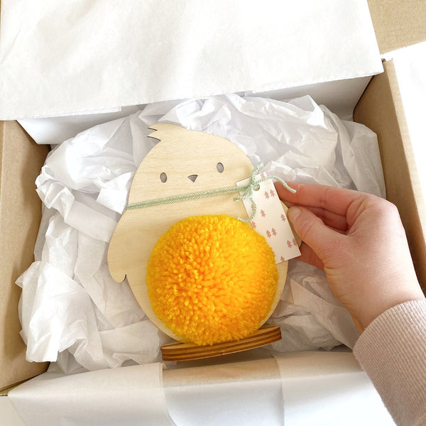 big pompom plywood chick with yellow pom pom being put into gift box