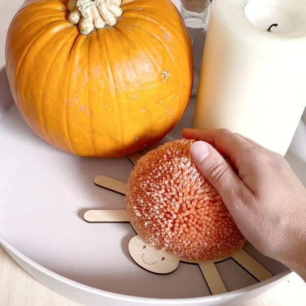 hand stroking pompom spider in peach next to orange pumpkin and white candle