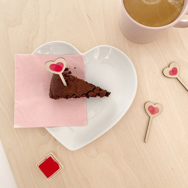 mini love heart treat topper in a slice of chocolate cake next to a cup of tea