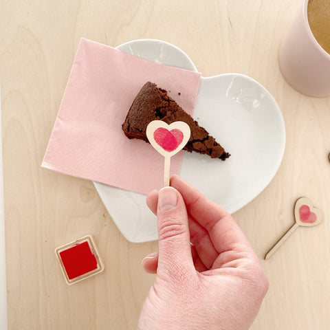 hand holding love heart treat topper with fingerprint and slice of cake